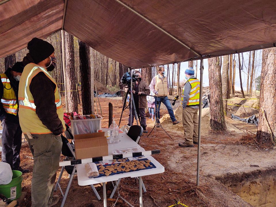 Field crew members on site, with recovered artifacts visible in the foreground.