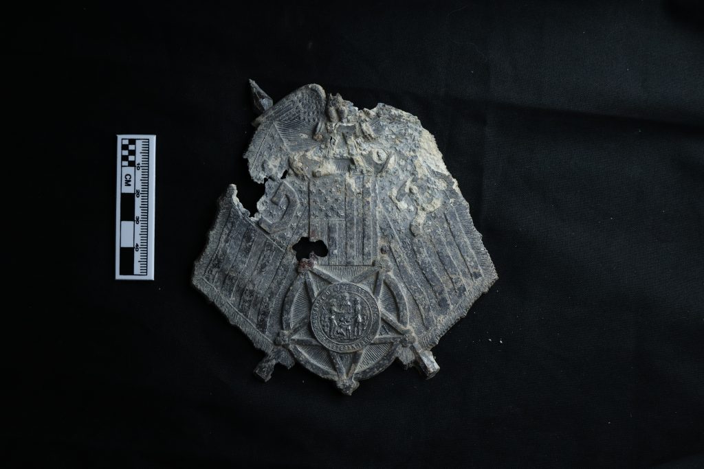 This white metal ornamental GAR coffin medallion was buried with one of the African American Civil War veterans who died and was buried in the national cemetery between 1890-1891. One benefit of membership for many chapters of the GAR was a fully paid funeral and burial in specially decorated coffins along with grave-side memorial services.